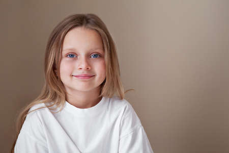 Pretty little girl blue eyes and long blonde hair wears white shirt isolated beige background. Caucasian beautiful fashion child model. Natural lightingの写真素材