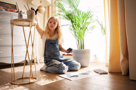 Child girl making drawings her hands on paper sitting on the floor. Young female artist painting with finger paints in living roomの写真素材