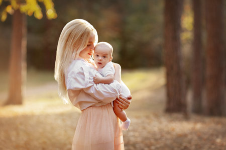 Mother Hugging her Baby. autumn landscape. Walk in nature outdoors. Family, motherhood, parenting and child care concept. Young blonde hair mom holding her child with loveの写真素材