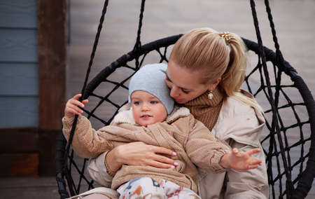 Beautiful Young Mom and baby hugging and have fun. mother holding her son. Models wearing knitted beige sweater, jacket, beanie. lifestyle portraitの写真素材