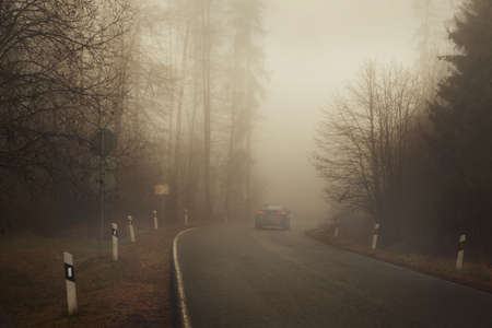 Alone Car is driving on road in the fog. Dangerous turn in bad weather conditions, poor visibility. mystical natureの写真素材