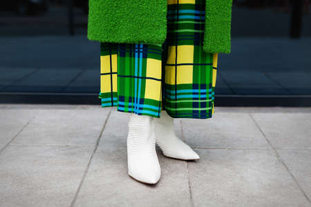 Close up Woman legs wearing stylish elegant leather white shoes with heels, green coat, yellow plaid...