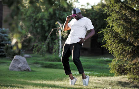 African American man dancing outside in nature park. Dancer wearing white T-shirt, black trousers...