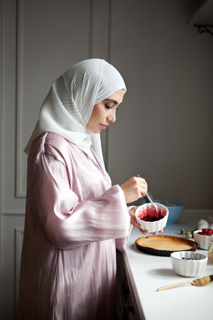 Side view portrait Muslim woman cooks dessert cake at kitchen, arabian young model in hijab and abaya. islamic traditional clothingの写真素材