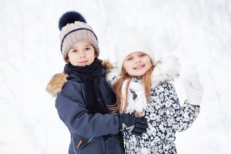Portrait of beautiful cheerful children on white snow background. Pretty Models wearing winter...