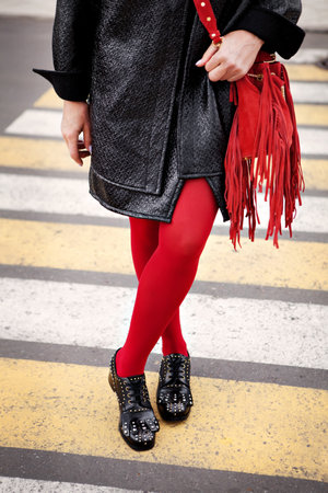Woman in red color tights, black shoes with rivets and hand bag with fringe standing on pedestrian crossing. Fashion details for stylish extravagant womenの写真素材