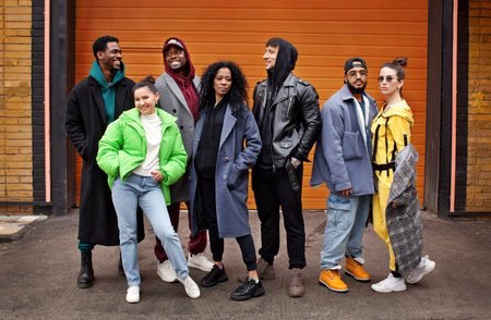 Multiracial group of young friends together on city street against orange colorful background....