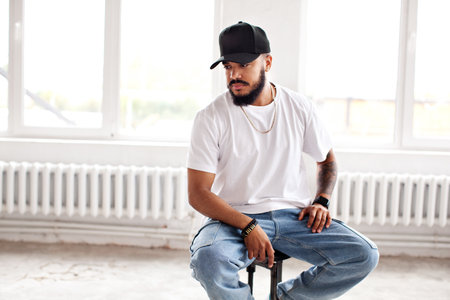 Authentic Portrait bearded man sitting in white loft background, looking away, wearing casual white...