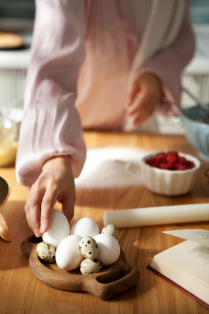 Close-up hand taking egg for kneading dough in kitchen. Woman bakes pie or cake at homeの写真素材