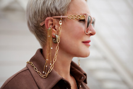 Close up portrait of woman wearing fashion accessories and jewelry, glasses on gold chain, earrings and clips, side viewの写真素材