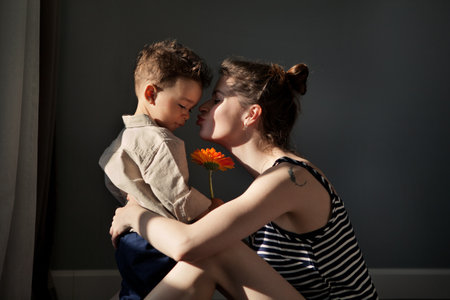 Real moment stylish Child Son gives mother gerbera flower for happy mothers day against dark wall....