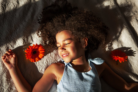 Peaceful young African American girl with closed eyes lies on bed with stunning orange Gerbera...