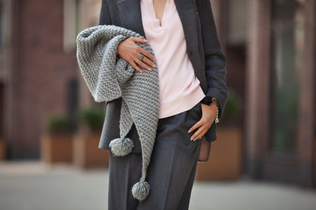 Midsection of unrecognizable woman wearing knitted warm scarf and gray wool business suit with jacket and trousers on city street, stylish color combination in clothesの写真素材