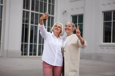Beautiful Senior women taking selfie photo on mobile phone at city, smile against background of white building. Two older female friends on vacation.の写真素材