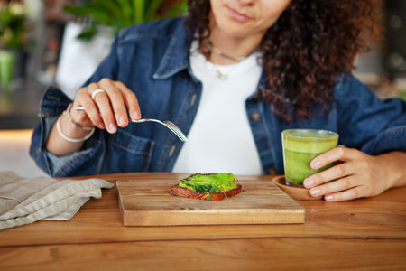 Woman enjoys avocado toast and green smoothie in a restaurant, showcasing vegan healthy food optionsの写真素材