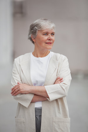 Professional in light business attire standing outdoors with arms crossed, displaying confidence against a bright background.の写真素材