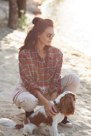 Beautiful brunette woman enjoys a serene moment with her dog outdoors, bathed in soft sunset light during a summer evening. Female owner with a pet in natureの写真素材