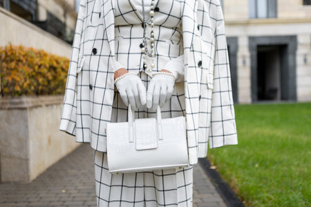 Fashionable Woman Standing Outdoors in City Dressed in Stylish Checkered White Suit with Blazer and Trousers, Leather Gloves and Handbag, Showcasing Details Trendy Clothing and Street Styleの写真素材