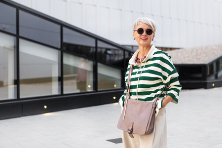 Portrait Beautiful Happy Mature Woman in Stylish Outfit Outdoors in the City with Short hairstyle Wearing Striped Sweater and Sunglasses, Looking at Camera. Gray Haired Senior Model Smilingの写真素材