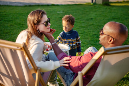 Happy Family holiday, Mother and Father With Child Enjoying Quality Time Together, Relaxing On Lounge Chairs On green Grass In Park On Warm And Sunny Day.の写真素材