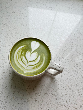 Overhead view of matcha latte in ceramic mug, featuring detailed latte art. The drink is on rustic stone surface, bathed in soft morning light for calm, inviting feelの写真素材