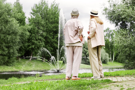 Two elderly women standing full length in park together, admiring beautiful natural landscape and enjoying active senior lifestyle, friendship and peaceful retirement outdoors at summerの写真素材
