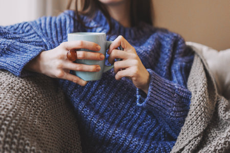 Woman relaxing on sofa, drinking warm cup of coffee or tea. Cozy home comfort, hygge lifestyle. Leisure, rest, weekend in winter or autumnの写真素材