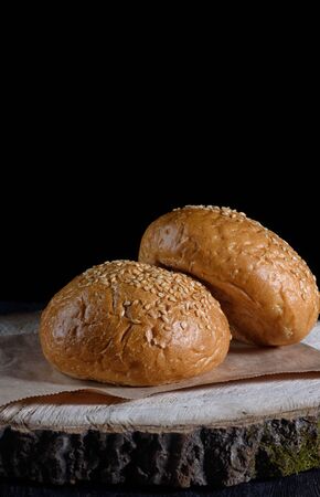 Two hamburger buns lie on a wooden board on a black background