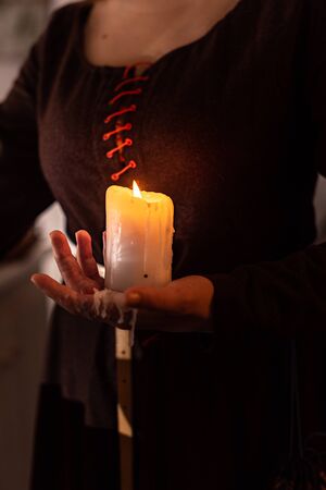 woman in the image of a witch in an old dress holding a burning candle in her handsの写真素材