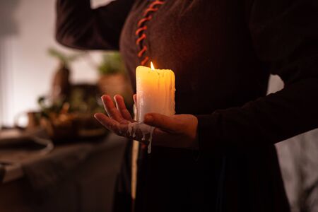 woman in the image of a witch in an old dress holding a burning candle in her handsの写真素材