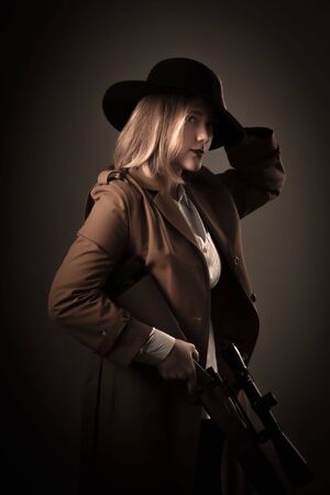 Mafiosi woman in a brown cloak and black hat with airguns in her hands. Gangster style photo shoot....