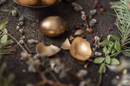 Golden easter eggs are scattered on a dark background with dry green branches. eggs in a golden bowl.の写真素材