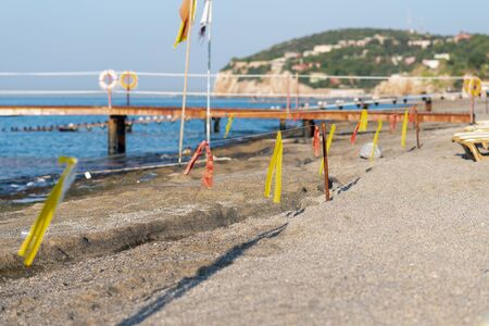 Boundary line of yellow and red ribbons on the beach against the background of the old pierの写真素材