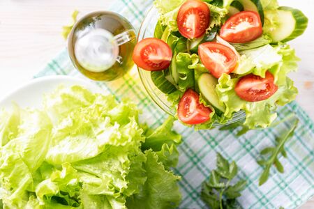 slices of tomatoes and cucumbers in a cup with salad and olive oil on a checkered green towel. view from aboveの写真素材