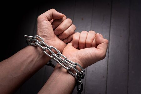 male hands on a gray background wrapped in a metal chain. prison conceptの写真素材