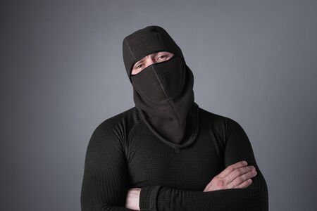 A man in a balaclava, as a special forces concept, stands with a menacing look, clasped hands on his chestの写真素材