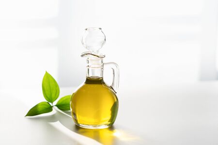 vegetable olive oil in a decanter on a white background next to a green leafの写真素材
