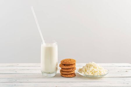 on a white background a stack of oatmeal cookies and cottage cheese, next to a glass of milk with strawsの写真素材
