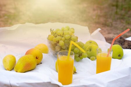 Outdoor breakfast at the beach. Fruits - grapes, pears, apples and orange juice on a white tableclothの写真素材