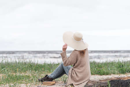 Woman looking at the beach during a storm, wearing a warm cardigan and beige hat..の写真素材