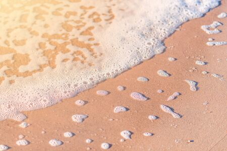 sea â€‹â€‹foam from the surging wave lies on a sandy beach
