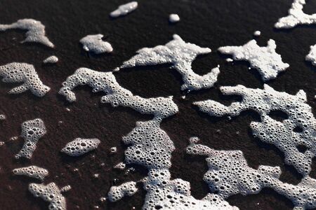 a white foamy wave surges onto a sandy beachの写真素材