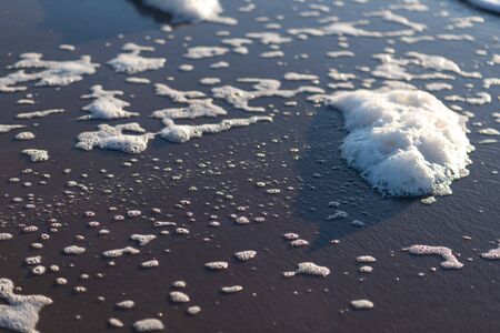 a white foamy wave surges onto a sandy beachの写真素材