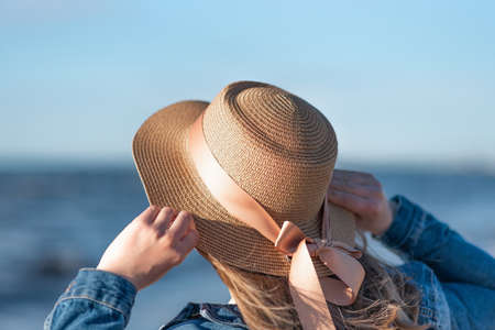 woman in a straw hat and denim jacket on a background of the sea. Close up rear viewの写真素材