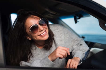 Happy young brunette smiling from the window of a white car on a background of blue sea.の写真素材