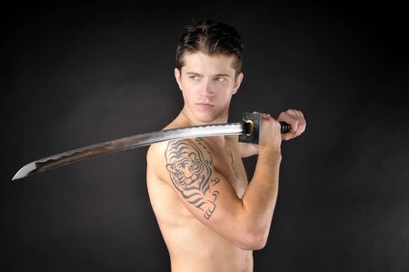 Athletic man with sword - isolated on dark background.の写真素材