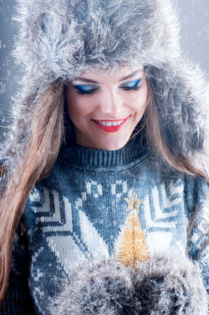 Winter fashion portrait of young smiling girl in fur hat and mittens, holding small decorative fir-tree.の写真素材