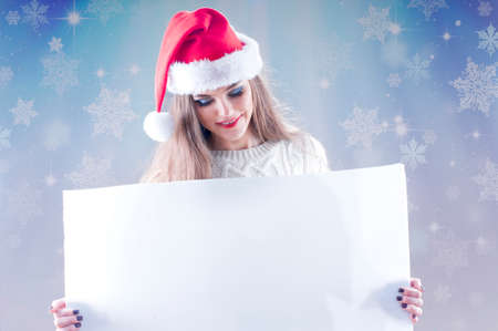 Happy young christmas girl holding a blank paper sign, isolated on snowy background.