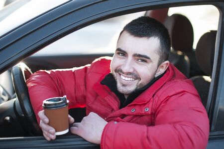 Attractive man in his  car drinking coffee outdoors.