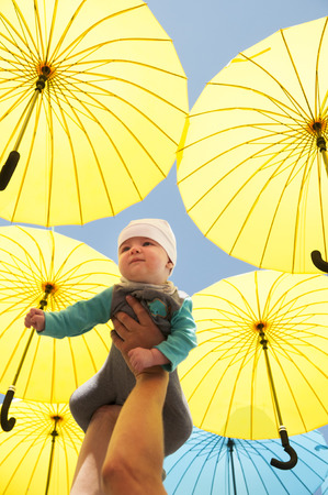 Newborn baby in her arms raised under a yellow umbrellas.の写真素材